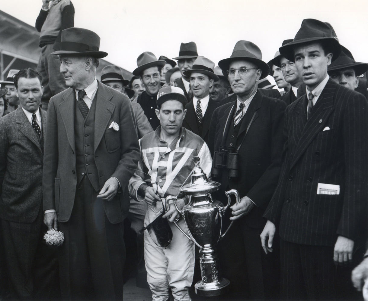George Woolf and Tom Smith hold the Pimlico Special trophy with Alfred G. Vanderbilt on the right and owner Charles S. Howard on the left (Keeneland Library Morgan Collection/Museum Collection)